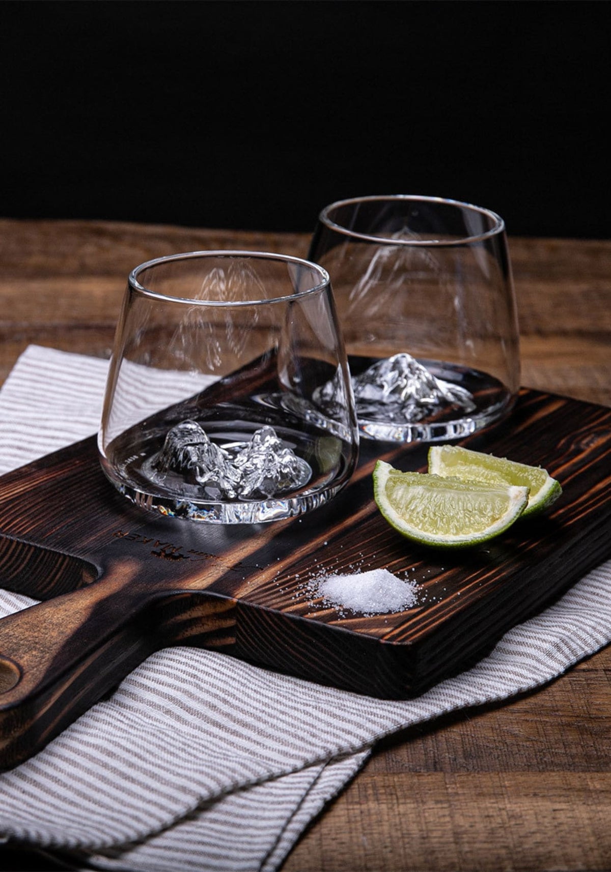 Les deux verres topographic Alaskan Maker sont posé sur une planche en bois avec deux quartiers de citron à côté en vue d'un cocktail
