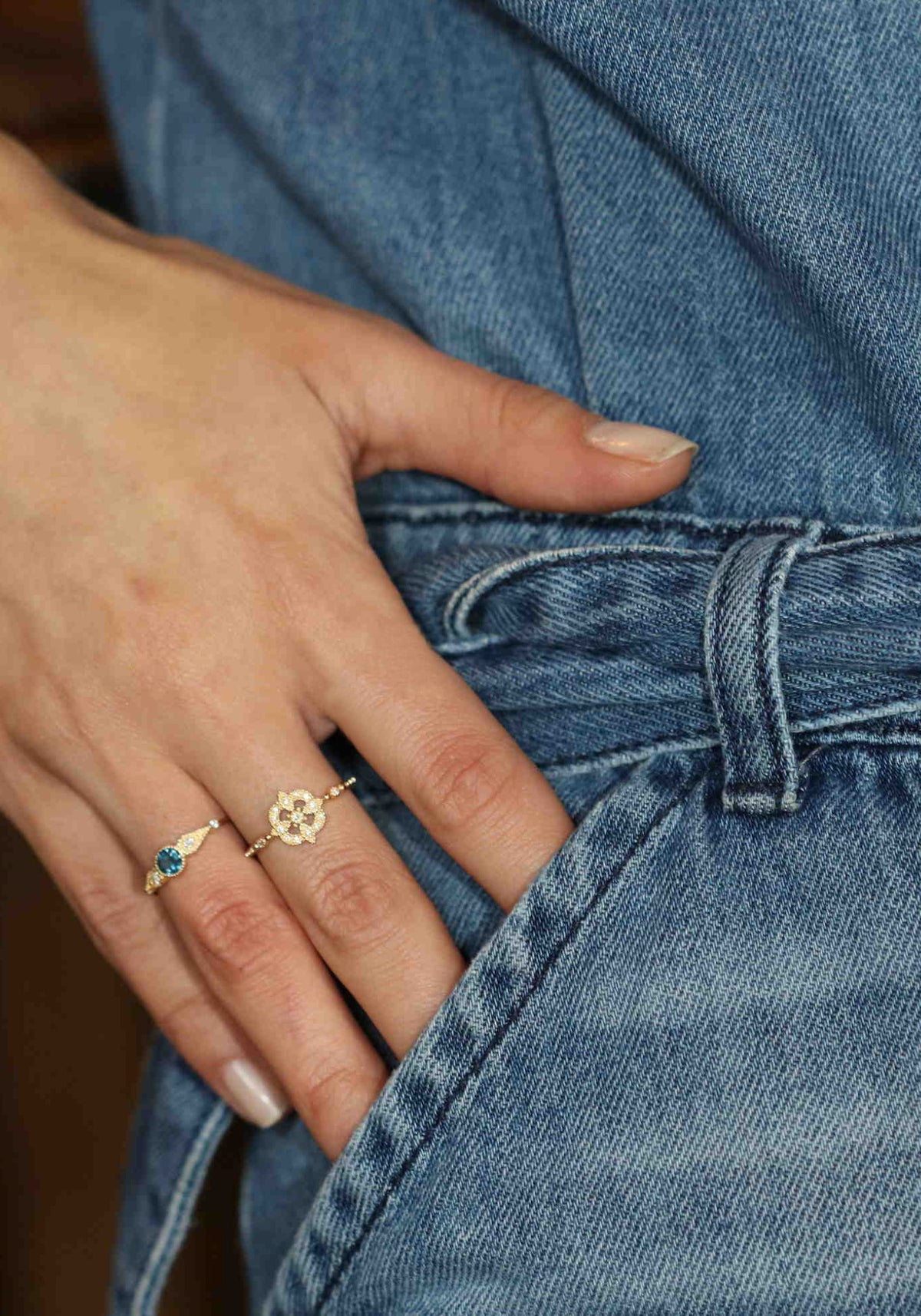 La femme a le bout des doigts dans la poche de sa combinaison et porte la bague en or jaune Gina Star de chez Angèle Brousse à son majeur