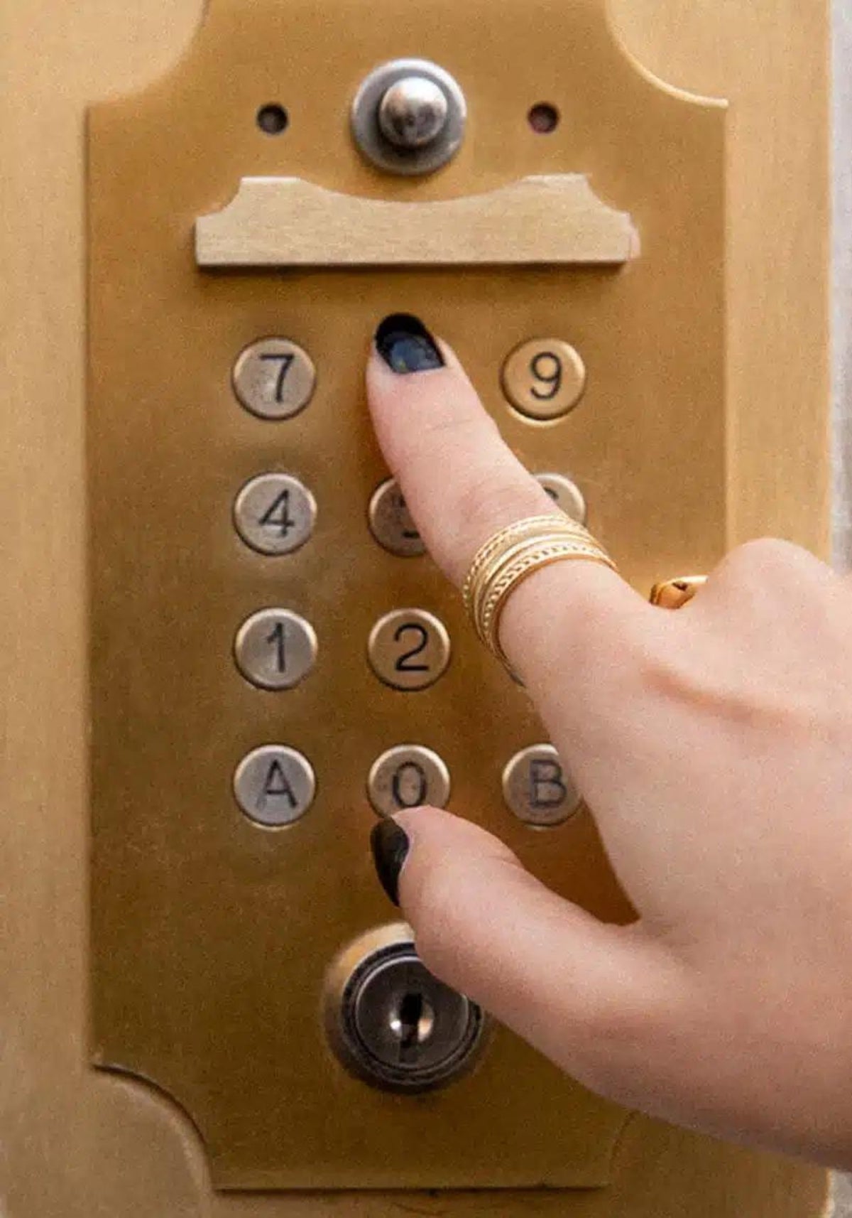 La femme appuie sur une touche d'un interphone et porte la bague Sabrina en or de chez Caprice Paris