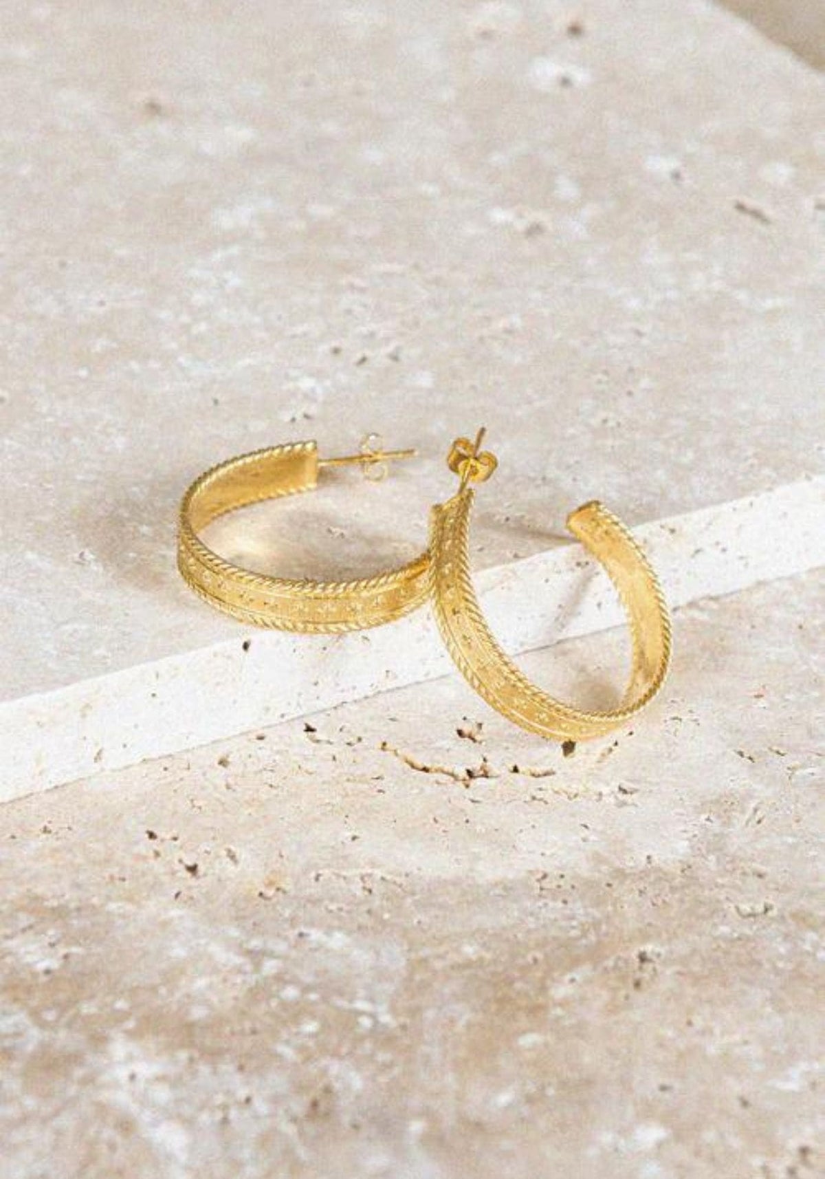 Les boucles d'oreilles Chiara de chez Bacci Paris sont posées sur un socle en pierre