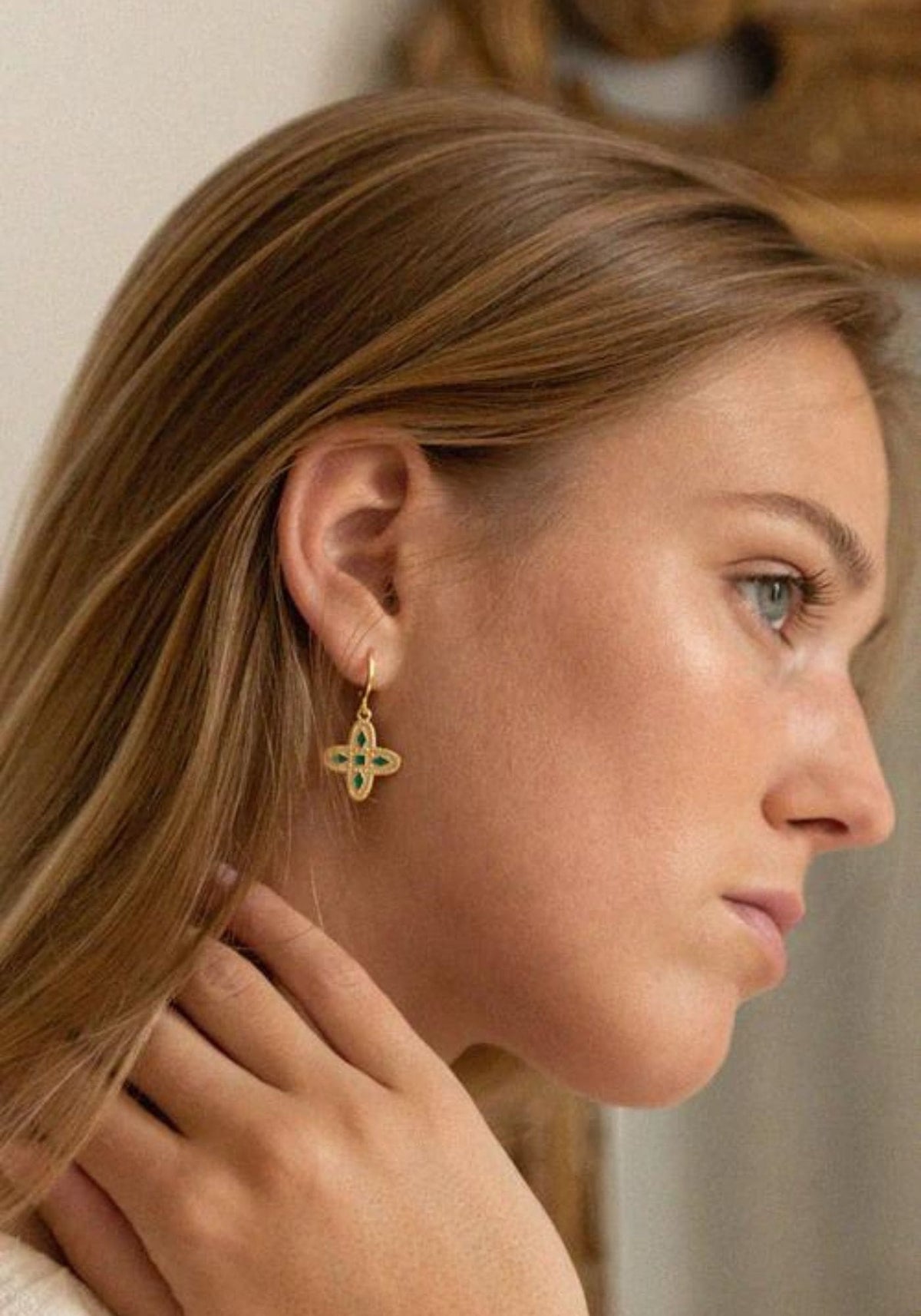 La femme porte des boucles d'oreilles Adriana vert émeraude de chez Bacci Paris