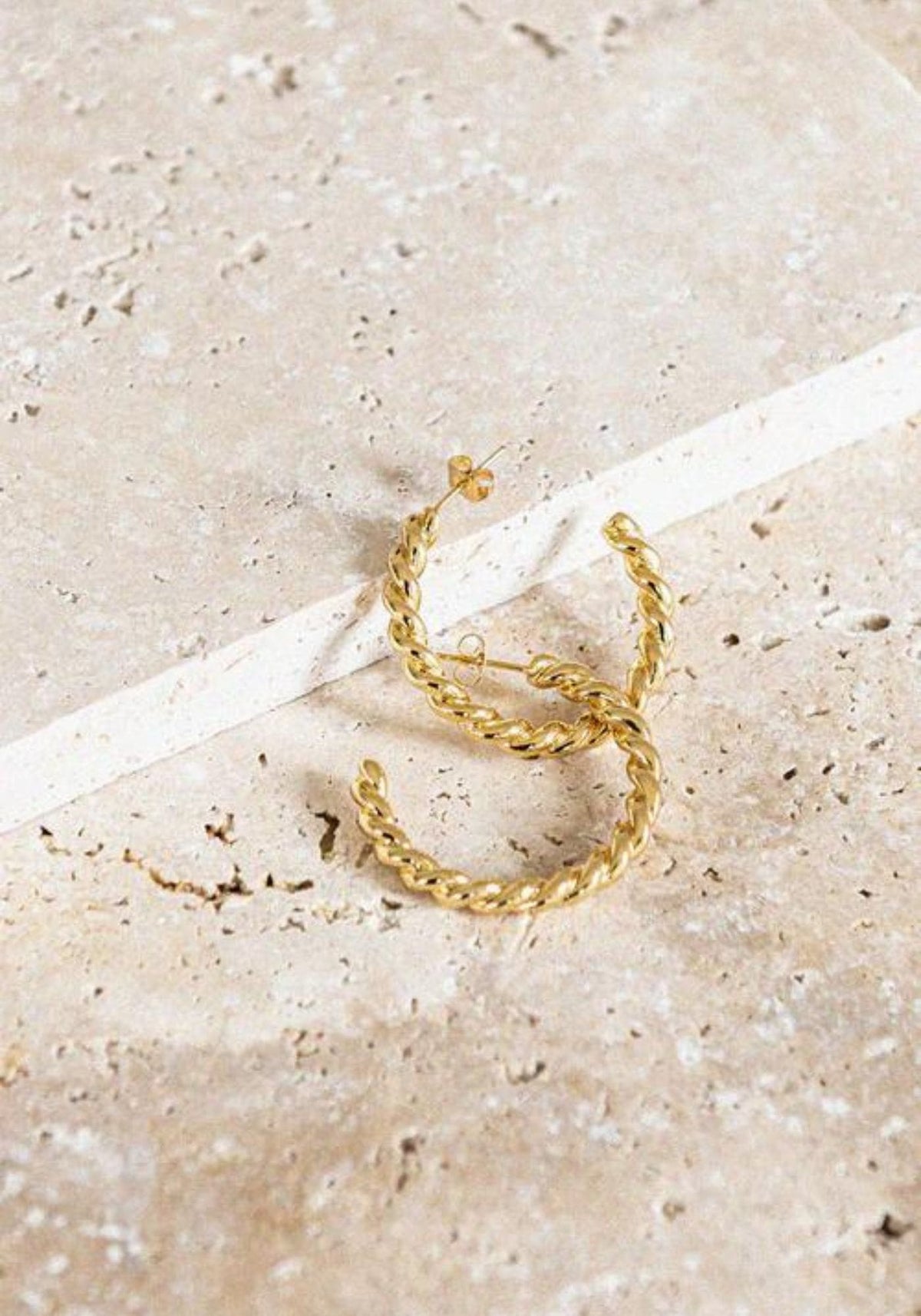 Les boucles d'oreilles Gabrielle de chez Bacci Paris sont posées sur un support en pierre