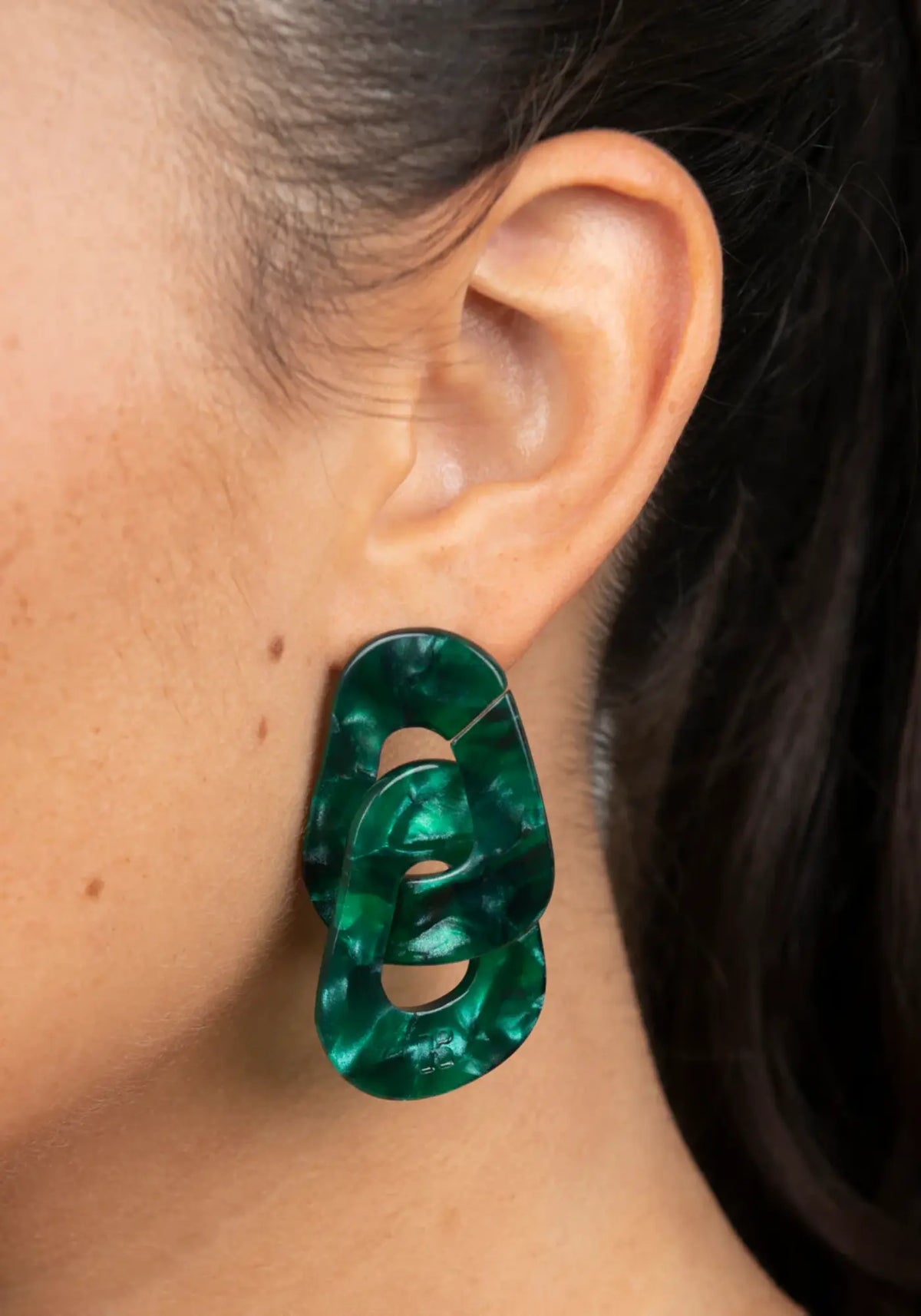 La femme porte les boucles d'oreilles maillon vert de chez Kurage Ginza