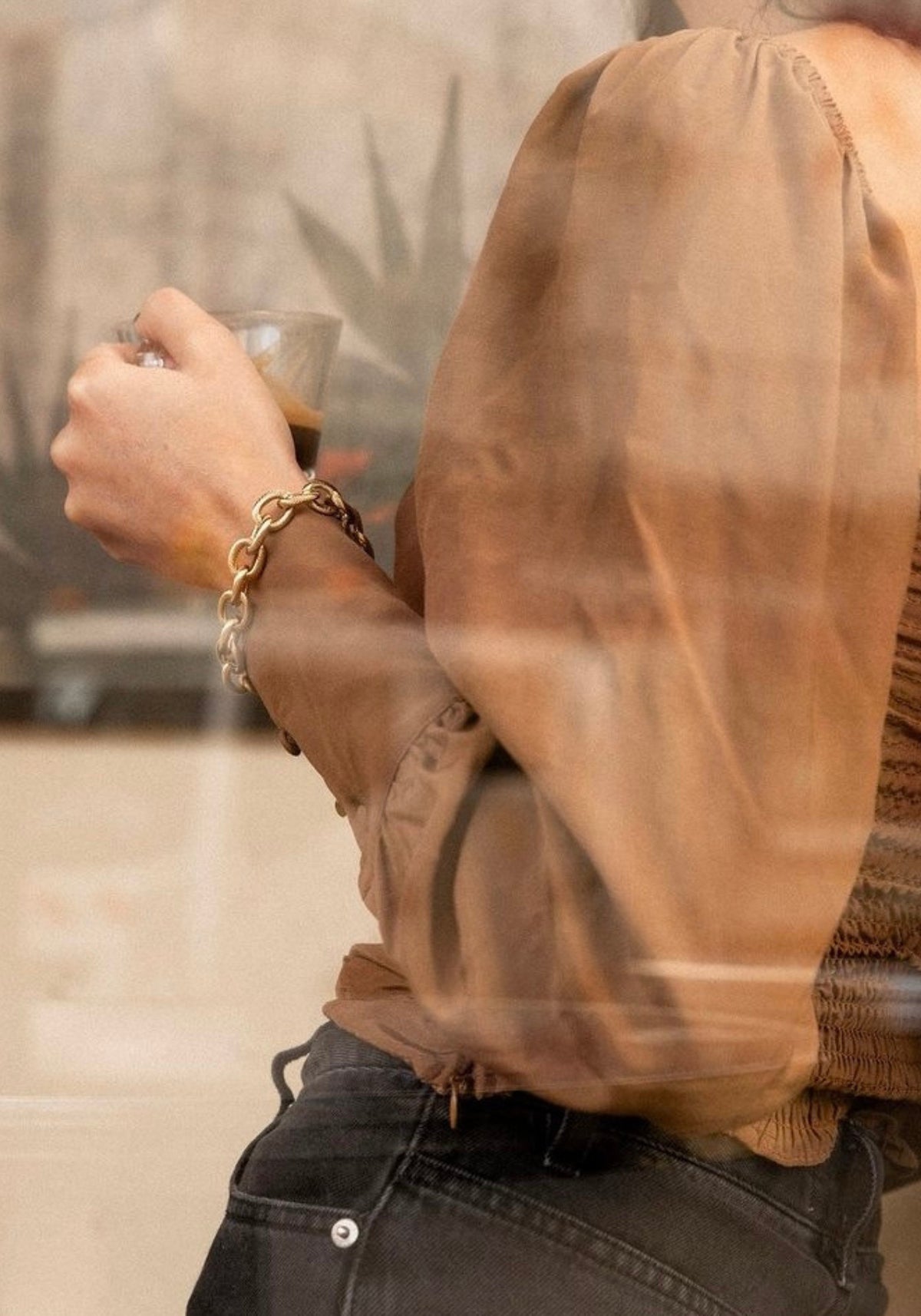 La femme boit un café en portant le bracelet en Grosse Maille Rita de chez Caprice Paris