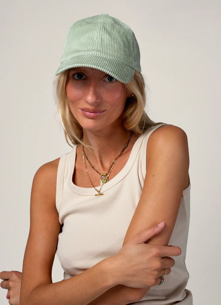 La femme porte la casquette en velours mixte vert pastel de chez Cotelé Paris 