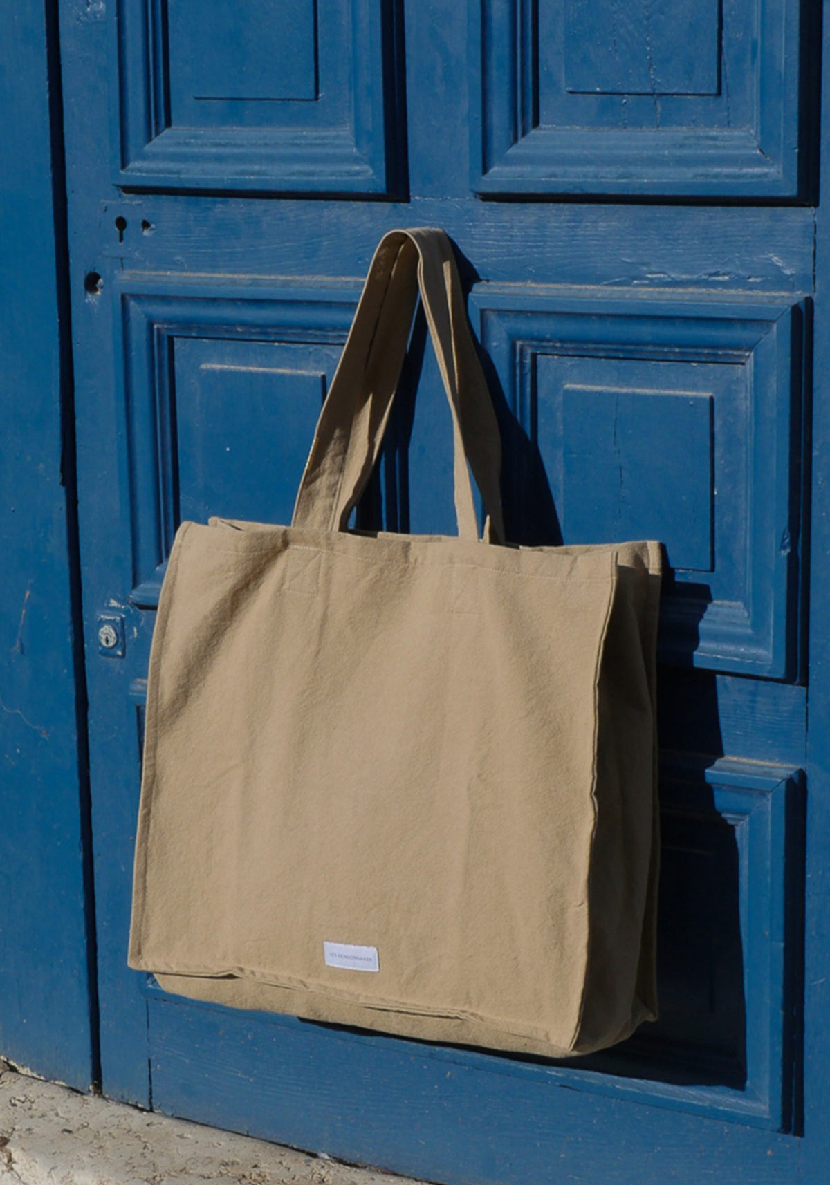 Le grand sac cabas beige sable de chez Les Pensionnaires accroché à une poignée de porte