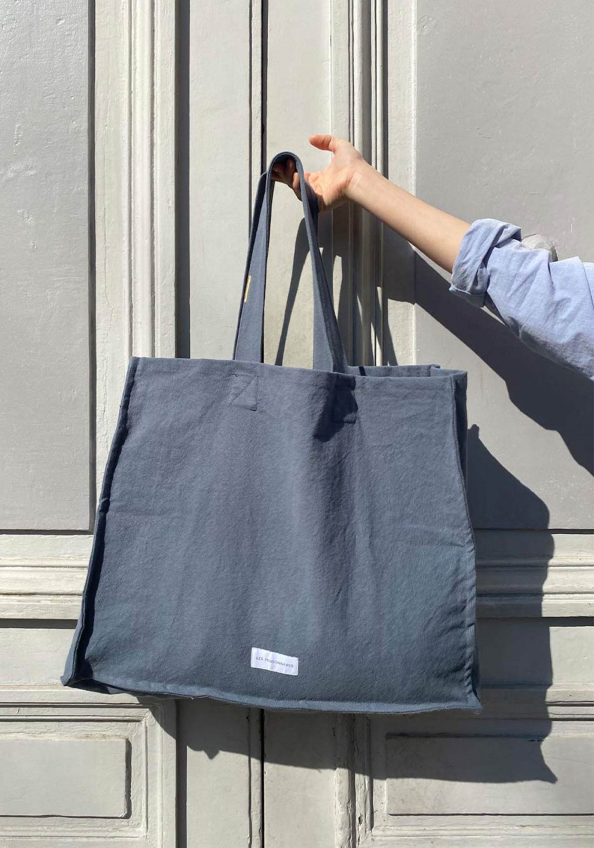 La femme tient le grand sac cabas bleu horizon de chez Les Pensionnaires