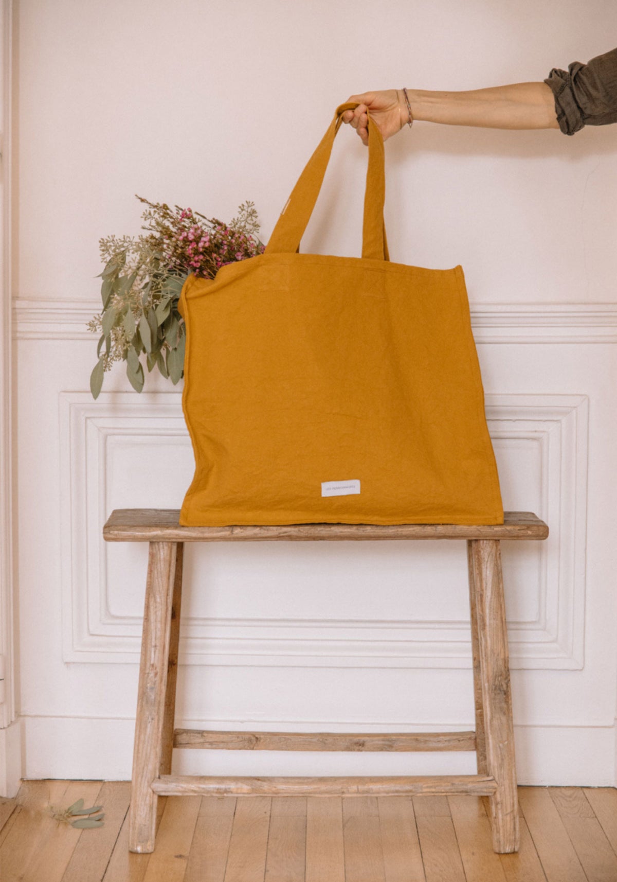 La femme tient dans sa main le grand sac cabas jaune safran de chez Les Pensionnaires posé sur un banc