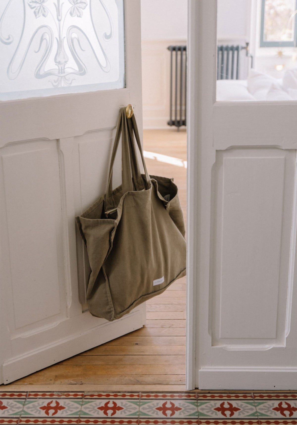 Le grand sac cabas tilleul de chez Les Pensionnaires suspendu à une poignée de porte
