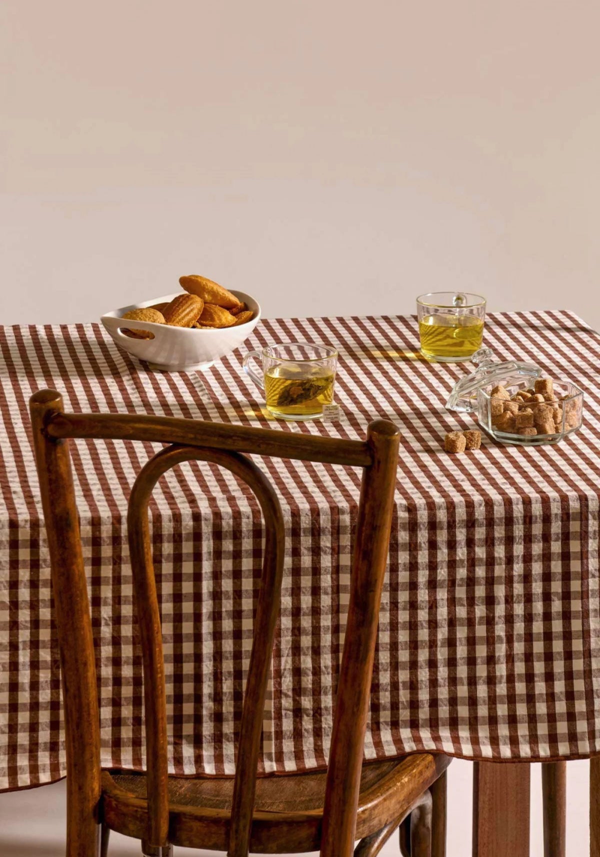 La nappe en lin et coton vichy noisette de chez Les Pensionnaires accompagnée de madeleines, tasses de thé et sucres