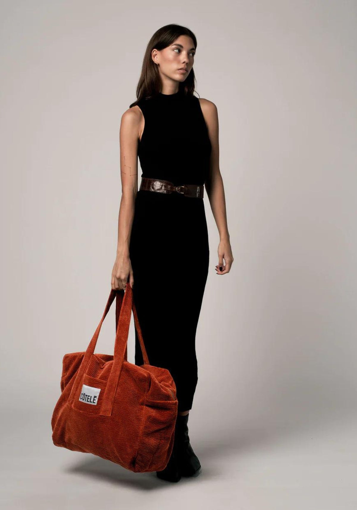 La femme porte le sac en velours week-end Bonny rouille de chez Côtelé Paris
