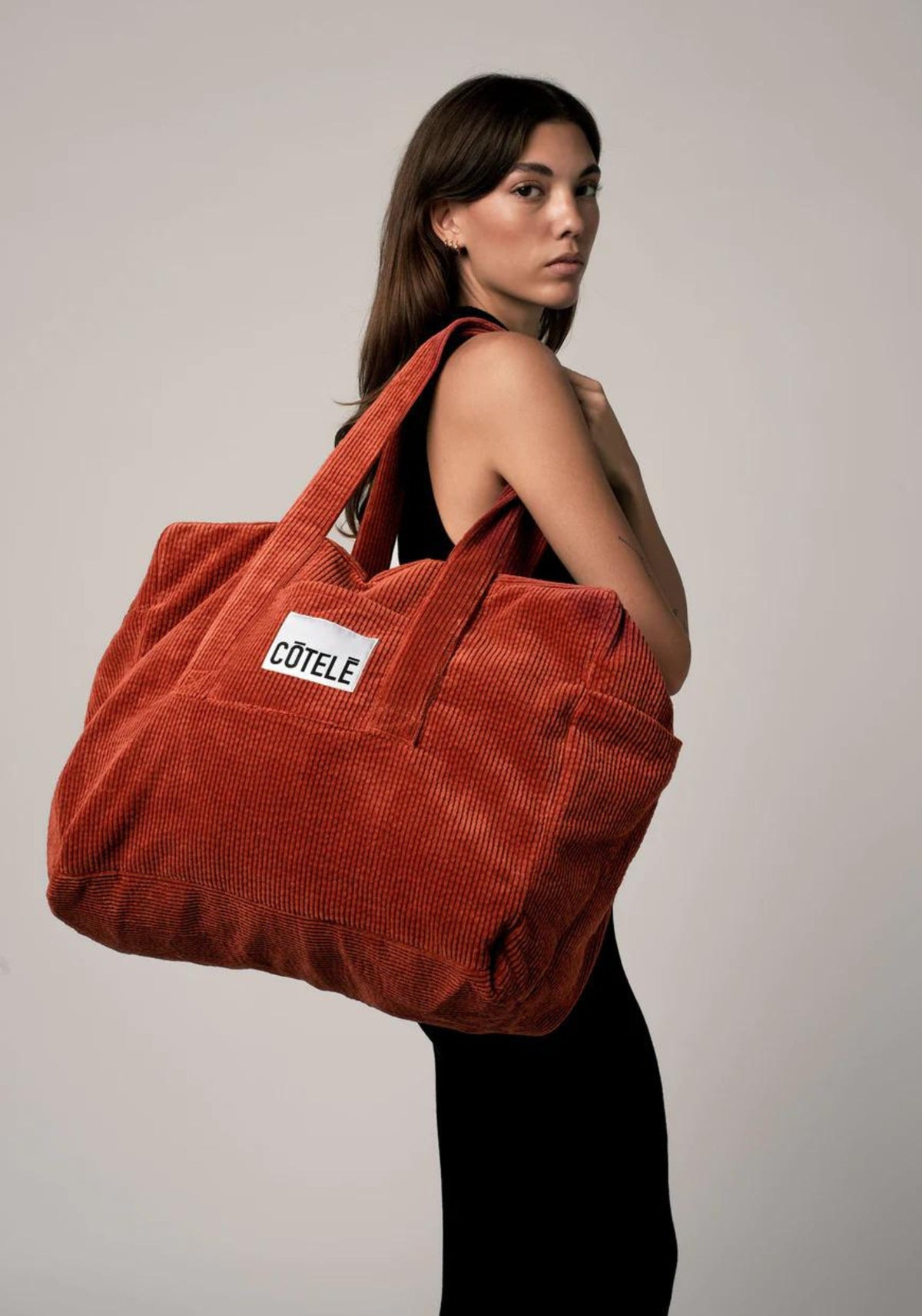 La femme porte le sac en velours week-end Bonny rouille de chez Côtelé Paris