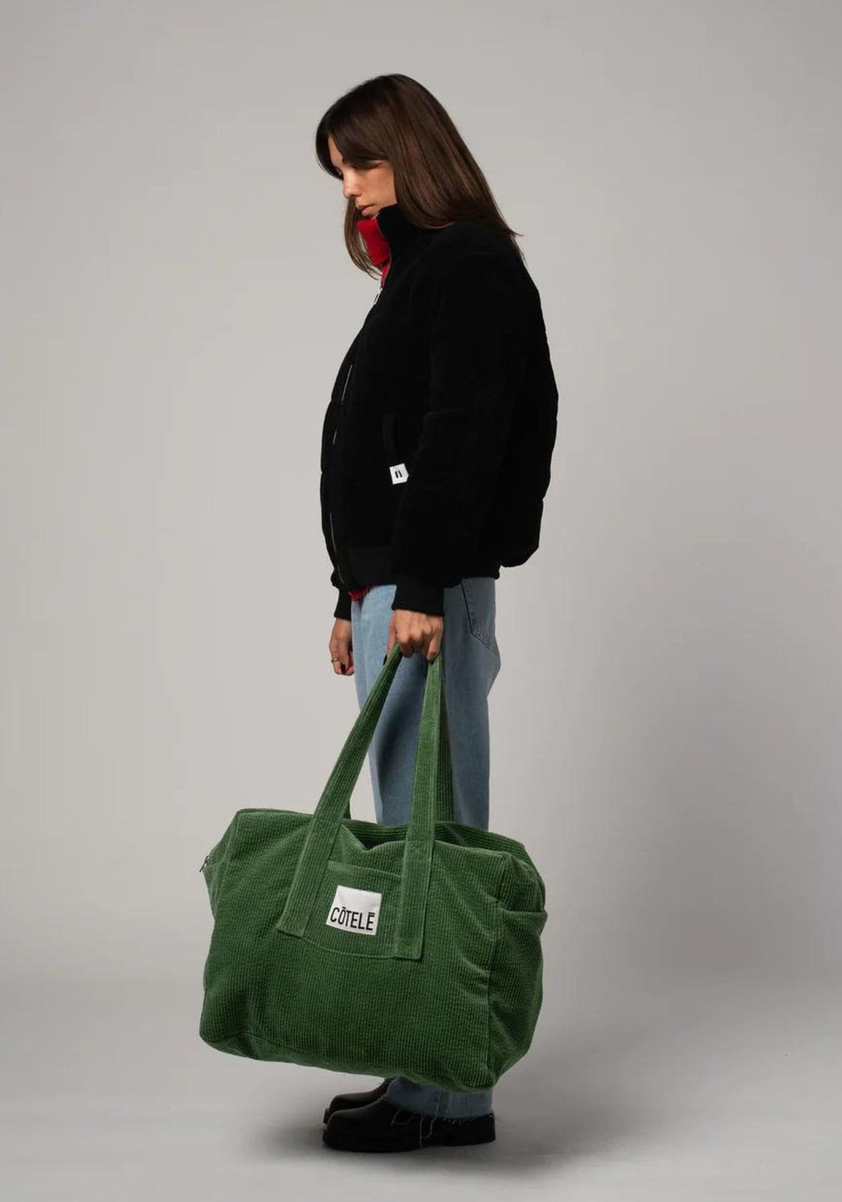 La femme porte à la main le sac week-end en velours de chez Côtelé Paris
