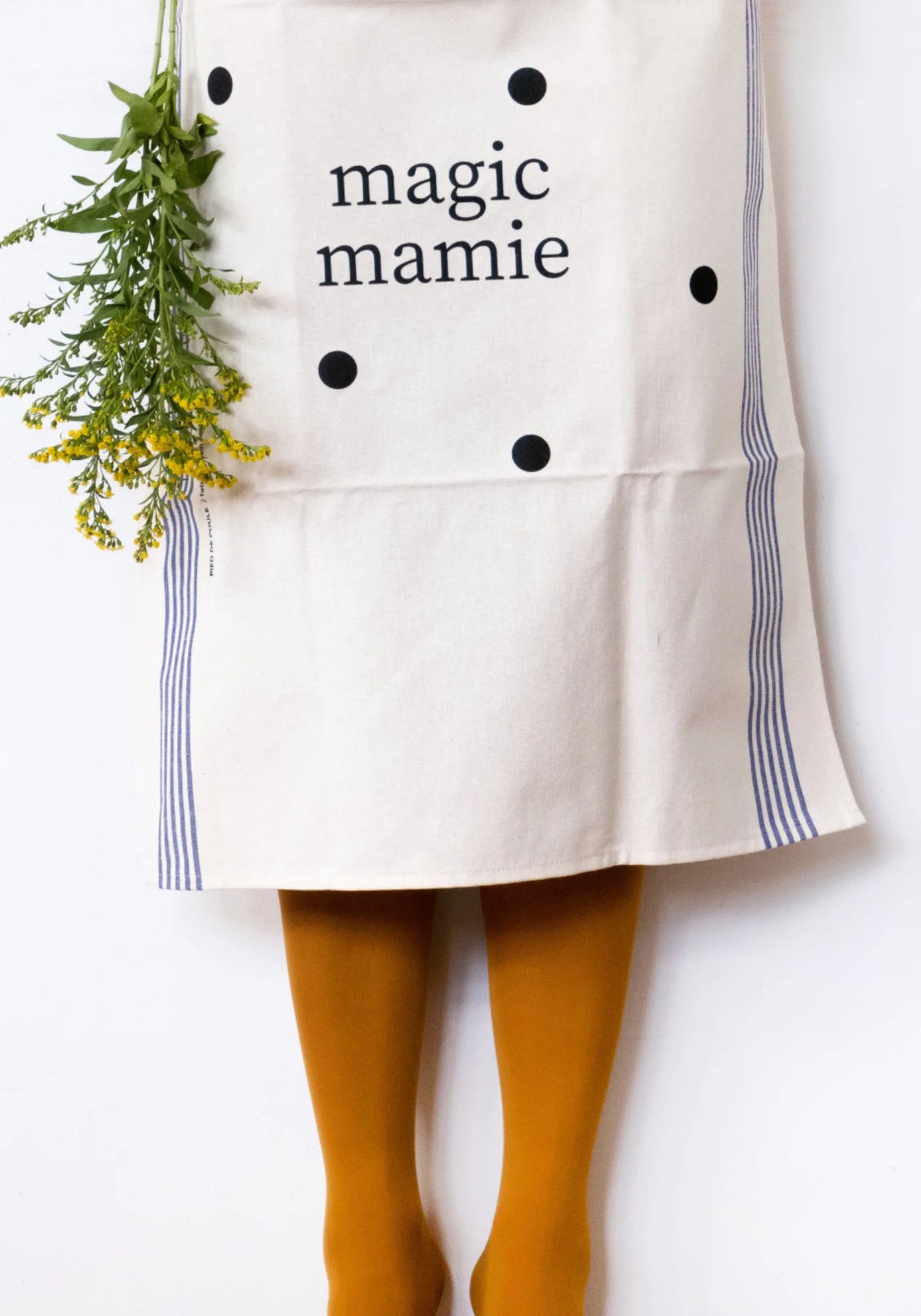 Le torchon en coton naturel Famille Magic Mamie de chez Pied de Poule accroché à la taille d'une dame avec un bouquet de fleurs