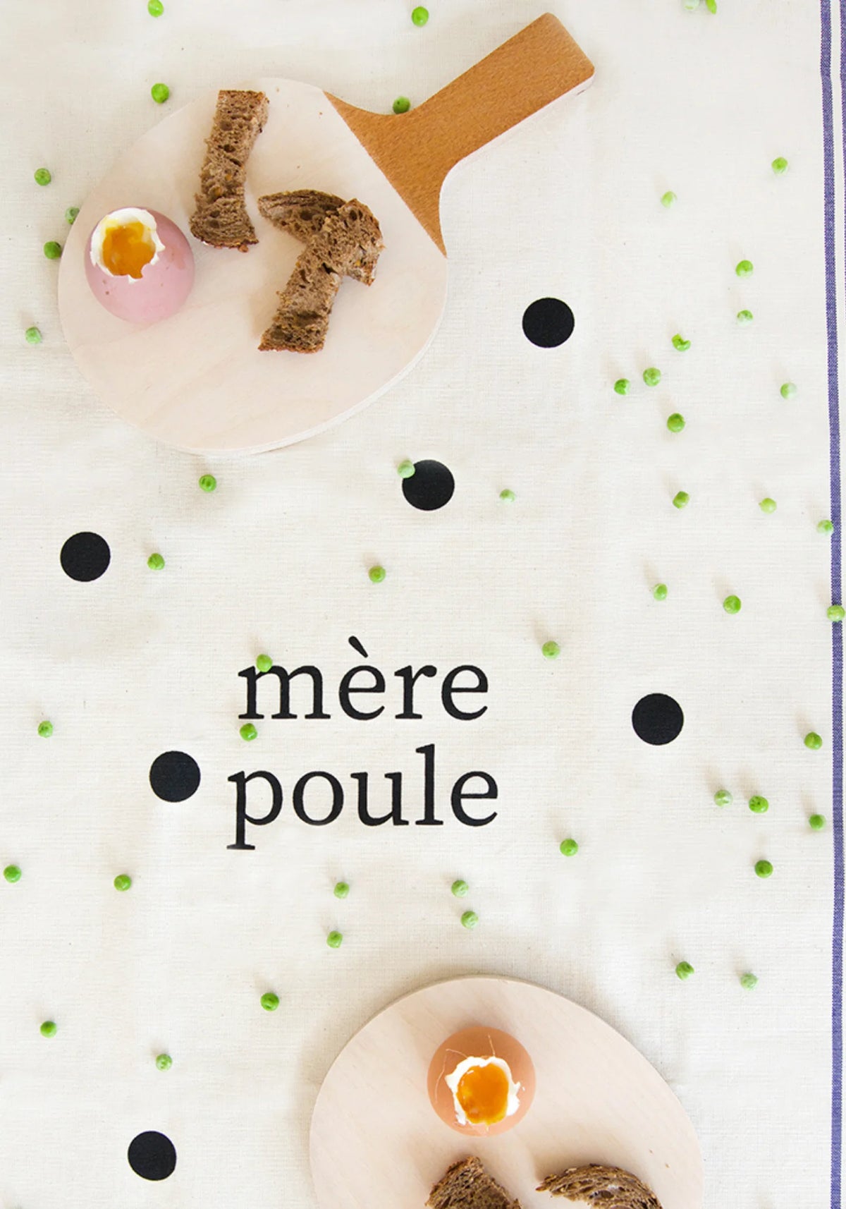 Le torchon en coton naturel Famille Mère Poule de chez Pied de Poule en guise de nappe. Posés sur le torchon, des oeufs durs avec du pain posés sur des raquettes de ping pong